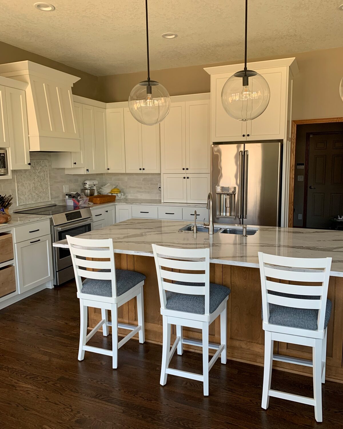 White painted kitchen with a stained island and three barstools