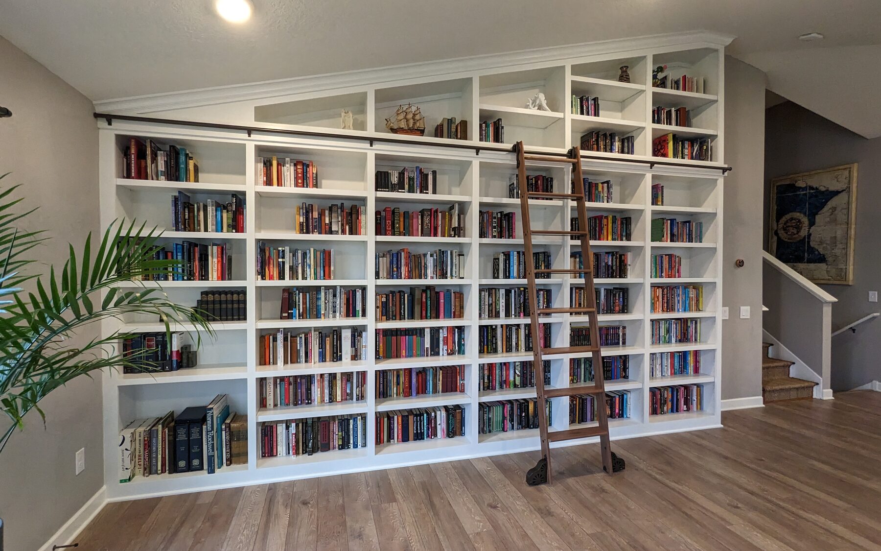 Floor-to-ceiling white library shelving with a rolling ladder under a vaulted ceiling