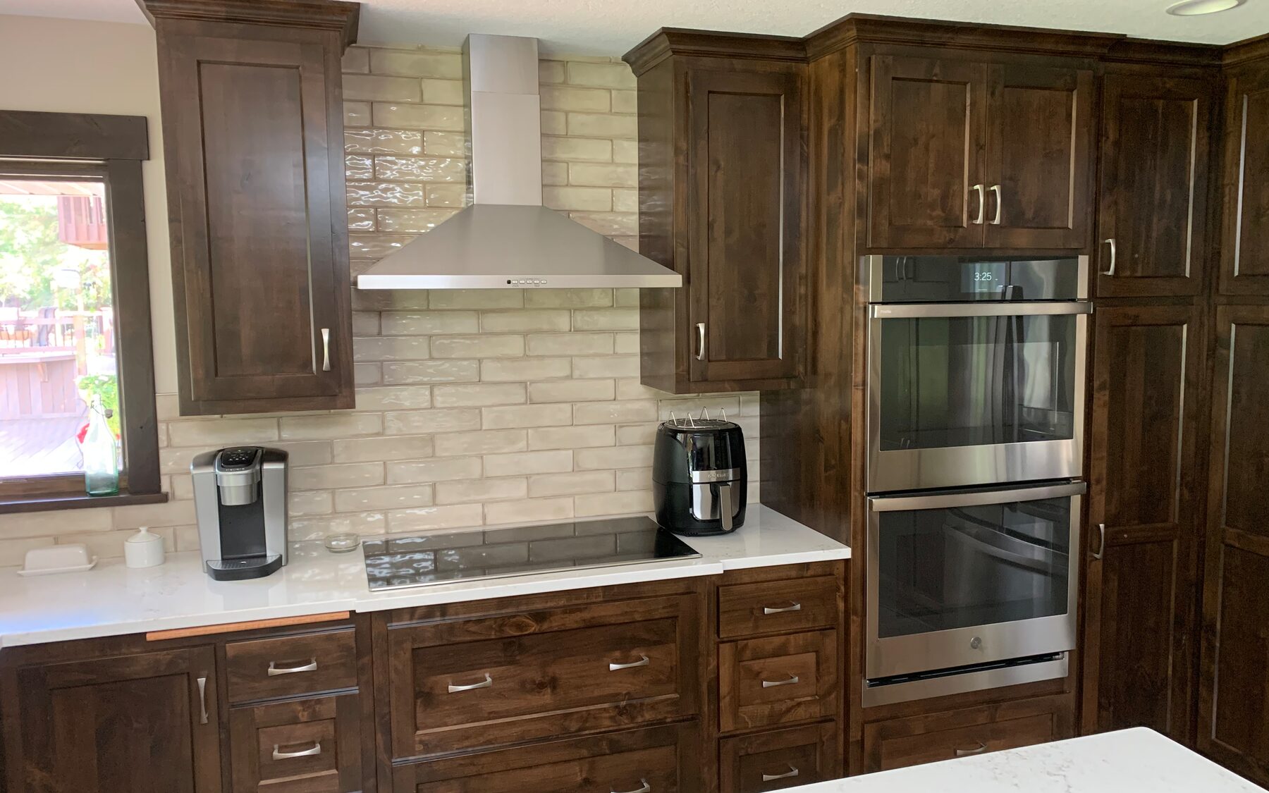 Dark stained kitchen cabinetry with double wall ovens and a tile backsplash