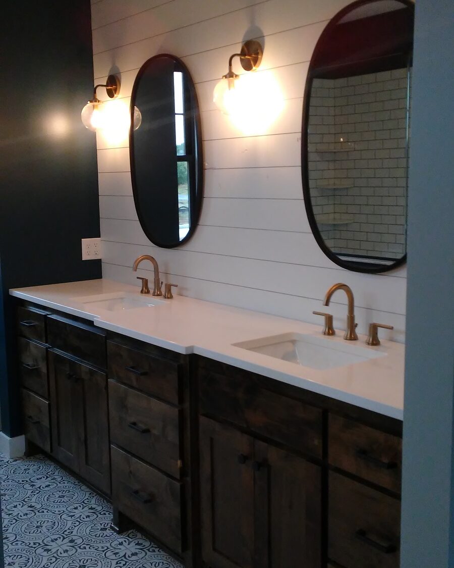 Dark stained double vanity below a shiplap wall with oval mirrors