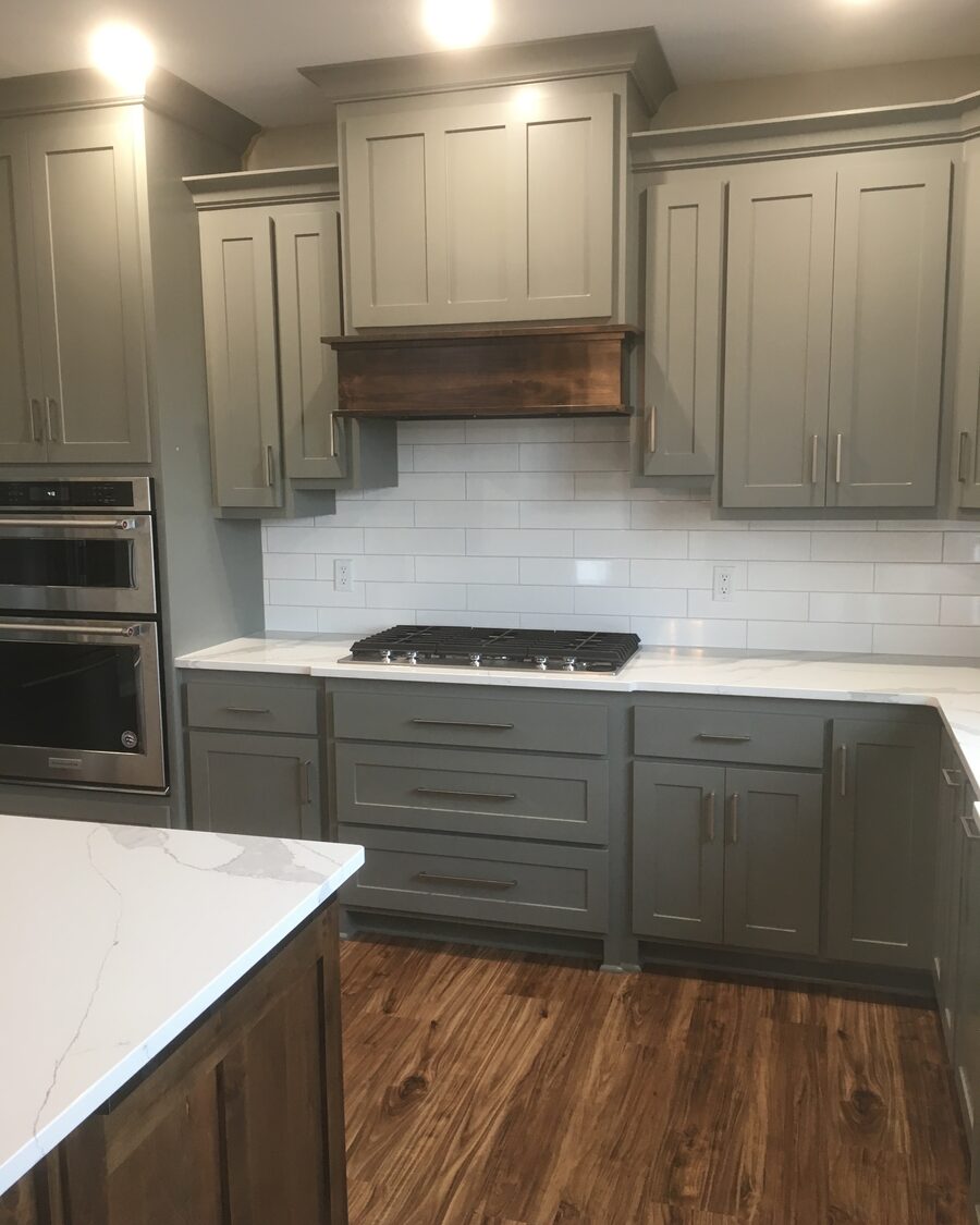 Gray painted kitchen with a stained wood hood band and subway tile